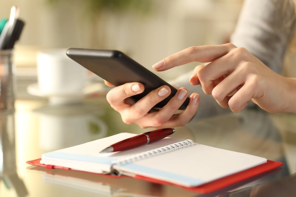 Image shows a person holding a mobile phone sat at a table